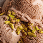 A serving of homemade chocolate and pistachio ice cream in a bowl with pistachios on top.