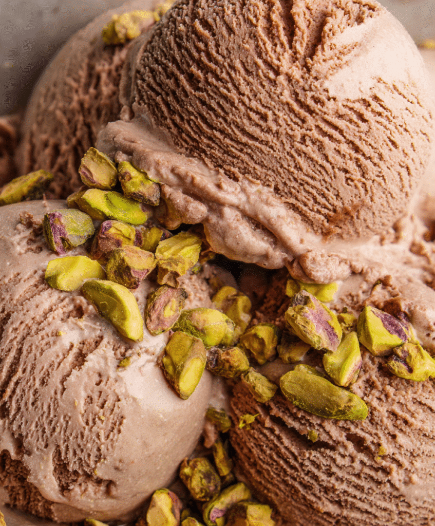 A serving of homemade chocolate and pistachio ice cream in a bowl with pistachios on top.