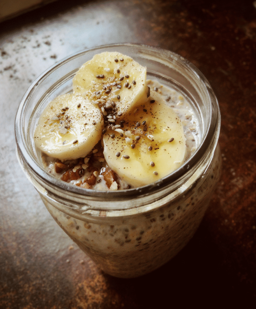 A bowl of overnight oats with banana and chia seeds, topped with fresh fruit and nuts.