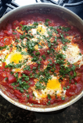 Shakshuka with Tomato Sauce in a skillet topped with poached eggs, fresh parsley, and crusty bread.