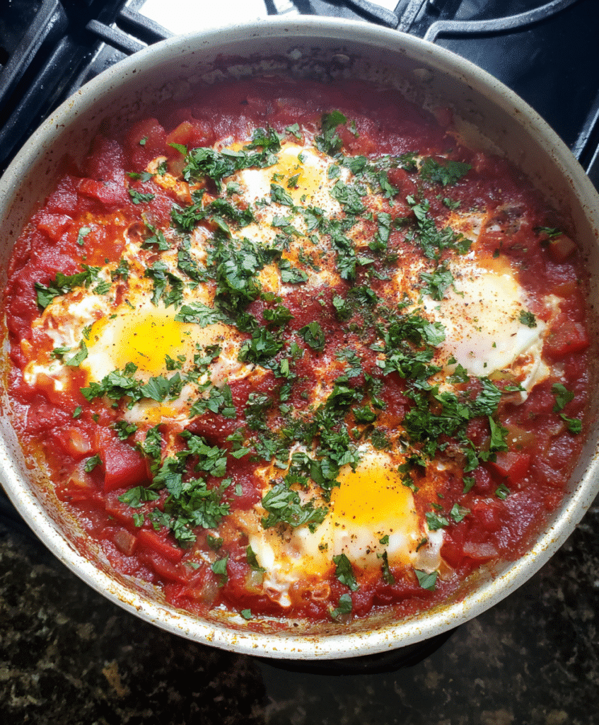 Shakshuka with Tomato Sauce in a skillet topped with poached eggs, fresh parsley, and crusty bread.