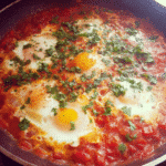 Ingredients for shakshuka with tomato sauce, including tomatoes, eggs, garlic, and spices.