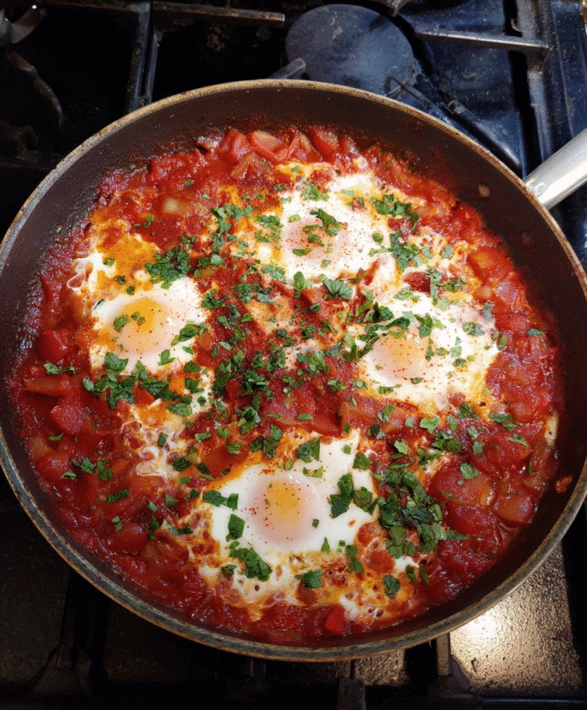 A bowl of shakshuka with tomato sauce served with crusty bread for dipping.

