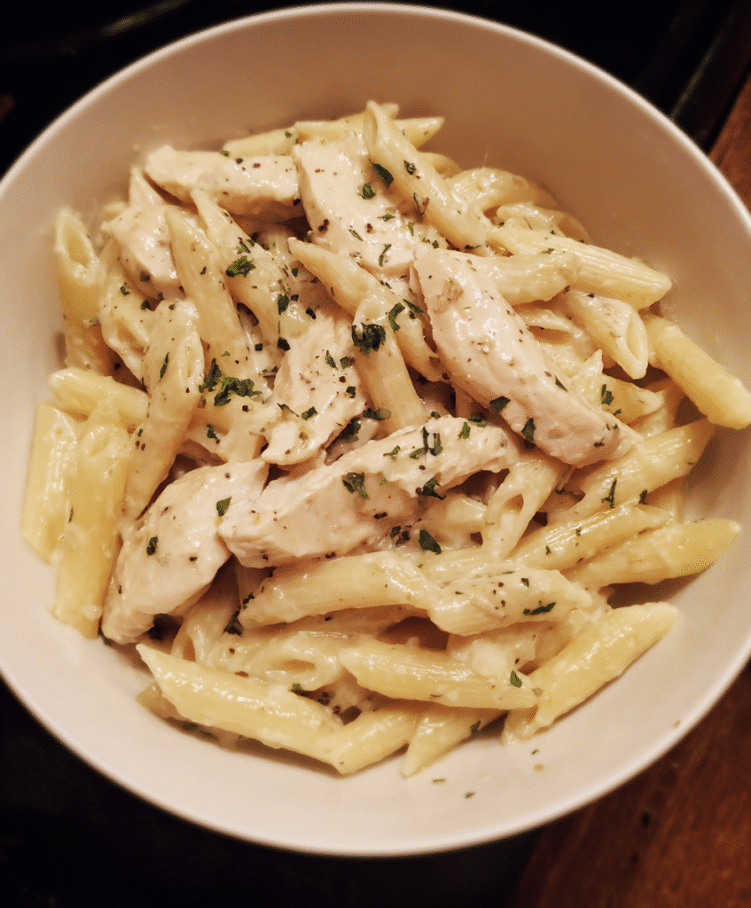 Plated Chicken Alfredo Penne Pasta with garlic bread and fresh salad.
